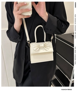 Close-up of cream mini crossbody bag with leather bow decoration and top handle