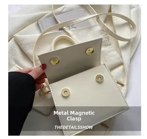 Detail view of the four golden magnetic closures and interior of the white square handbag