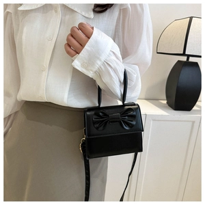 Dettaglio di una mini borsa squadrata nera con grande fiocco e tracolla regolabile