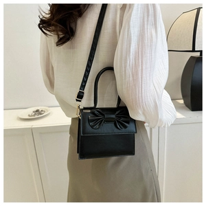 Detail view of a black leather mini square bag with bow tie on a female model