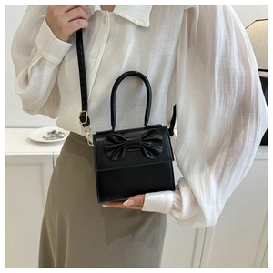 Detail of black mini PU crossbody bag with decorative bow and golden metal hardware