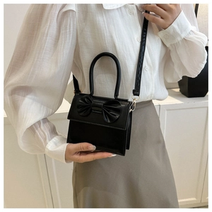 Detail of a black mini bow purse shown on model to demonstrate actual size and fit