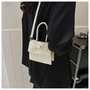 Detail of a beige bow-knot crossbody bag shown on a model in a black blazer suit