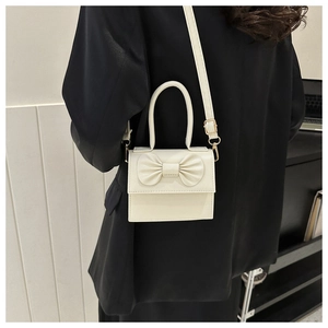 Dettaglio della mini borsa crema con fiocco che mostra texture e tracolla su blazer