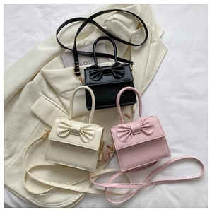 Dettaglio di tre mini borse con fiocco nei colori nero, crema e rosa su un blazer morbido