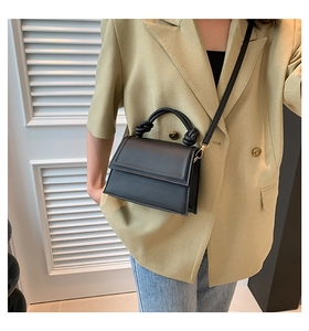 Detail of black square handbag showing knotted handle and gold metal hardware accents