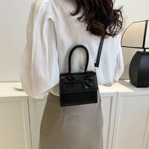 Mini borsa quadrata nera con grande fiocco indossata da una modella in un set minimal