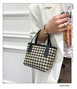 Detail of houndstooth pattern mini bucket bag with leather handles against white blazer