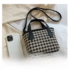 Detailed close-up of houndstooth tote bag with black faux leather handle and shoulder strap