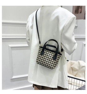 Detail of model wearing a black and white houndstooth bucket bag with white suit