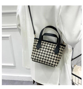 Detail of houndstooth tote bag worn with white blazer, showing crossbody strap and gold hardware