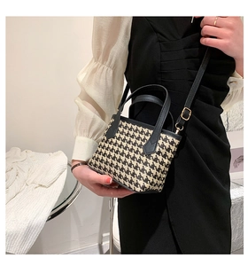 Detail of houndstooth bucket bag with black leather handle and adjustable shoulder strap