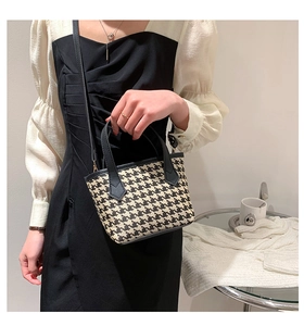Detail of houndstooth bucket bag featuring black leather handles and shoulder strap