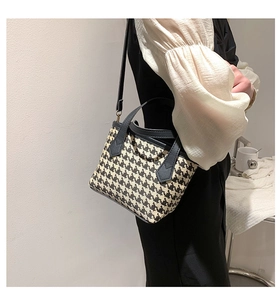 Detail of stylish houndstooth bucket bag worn as a shoulder bag with black strap