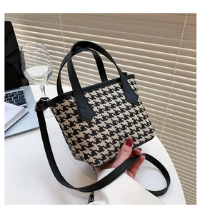 Detailed close-up of houndstooth tweed texture and leather handles on the bucket bag