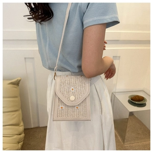 Detailed close-up of straw crossbody bag with daisy embroidery and woven texture