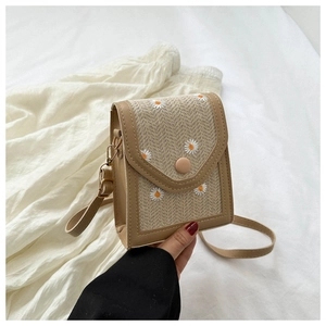 Close-up of woven small crossbody bag with embroidered daisies and faux leather trim