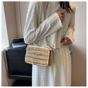 Detail of woven straw crossbody bag with brown leather patch and gold chain strap