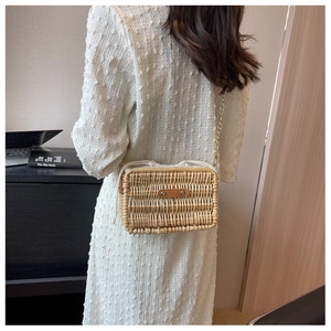Detail of woven rattan crossbody bag with brown leather patch and gold chain strap