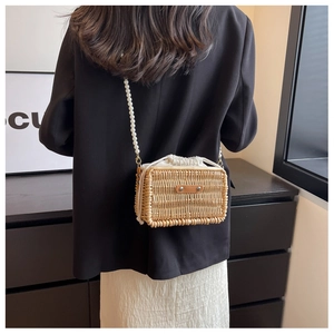 Detail of woven rattan bag with pearl shoulder strap and white drawstring lining on a model