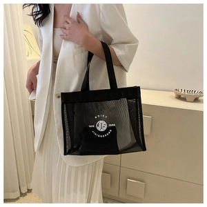 Detail of a large black mesh tote bag with white logo carried by a model in a white blazer