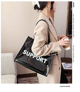 Detail of a transparent black PVC tote bag with white SUPPORT text held by a model