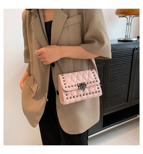Pink quilted shoulder bag with metal studs and chain strap on a khaki blazer