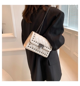 Close-up of off-white quilted chain bag with silver studs on a black blazer