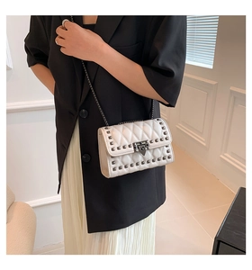 Detail of white quilted crossbody bag with metal studs and elegant chain strap on model