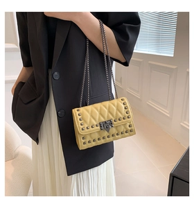 Detail of ginger yellow quilted bag with metal studs and chain strap on shoulder