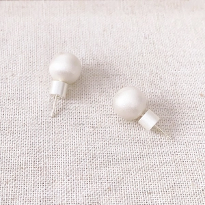 Elegant white round pearl earrings with brushed gold base on a textured fabric background