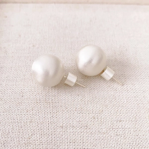 Minimalist round white pearl stud earrings with 925 silver needles on linen background