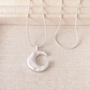 Minimalist silver moon pendant necklace with matte finish on textured jewelry tray