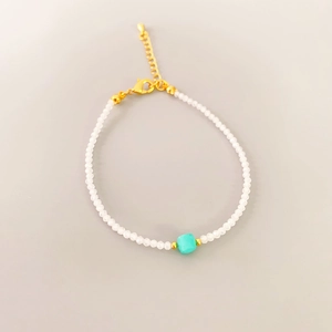Detailed shot of a handmade beaded bracelet with white beads and a turquoise square center