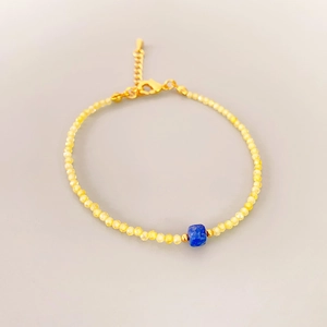 Macro view of dainty beaded bracelet with yellow faceted stones and blue square bead