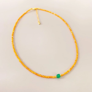 Detail of beaded necklace with orange faceted beads and a green square pendant