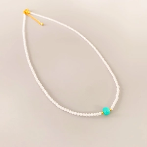 Close-up of beaded necklace with white translucent stones and a turquoise accent bead