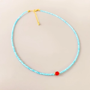 Minimalist sky blue beaded necklace with a central red square stone and gold clasp