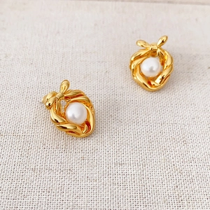 Elegant gold bow earrings featuring freshwater pearls set on textured beige fabric