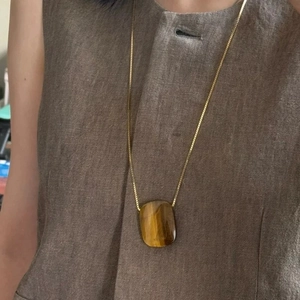 Close-up of tiger eye stone pendant on long gold box chain worn with linen clothing