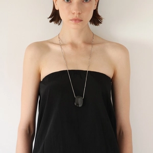 Detailed view of silver chain long necklace with dark rectangular gemstone pendant on model