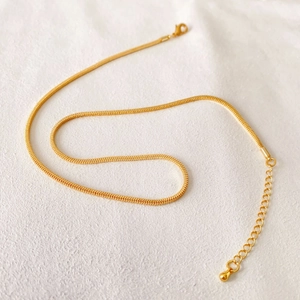 Minimalist gold plated snake chain necklace with lobster clasp on white textured background
