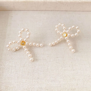 Elegant bow-shaped pearl stud earrings with zircon center on a textured beige tray