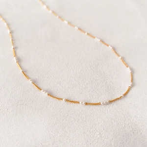 Minimalist gold brass chain necklace with white pearl beads on a soft textured background