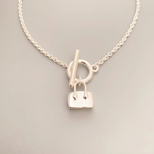 Detailed macro view of minimalist handbag pendant necklace with silver OT clasp buckle