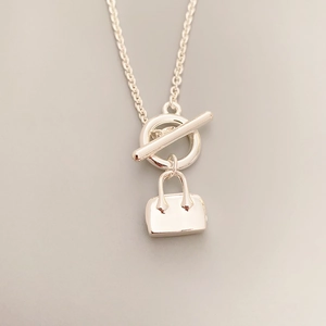 Macro view of silver necklace featuring an OT clasp and a miniature handbag pendant