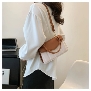 Detail of two-tone brown and white crossbody bag with knot handle and quilted texture
