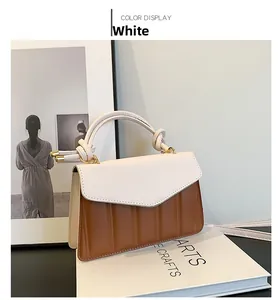 Detail of color-block handbag with white flap, brown base, and gold hardware accents