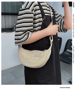 Detail view of beige nylon crescent bag worn on a model in a stylish outdoor setting