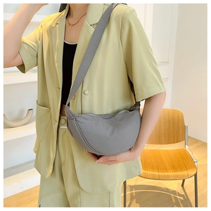 Detailed close-up of a grey nylon crescent crossbody bag worn by a model in a minimalist room
